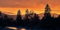 Dramatic golden hour sky reflecting off a rain-washed community road at Ridgewater Properties in Klamath Falls, Oregon, with silhouetted ponderosa pines and layered Cascade mountain ridges